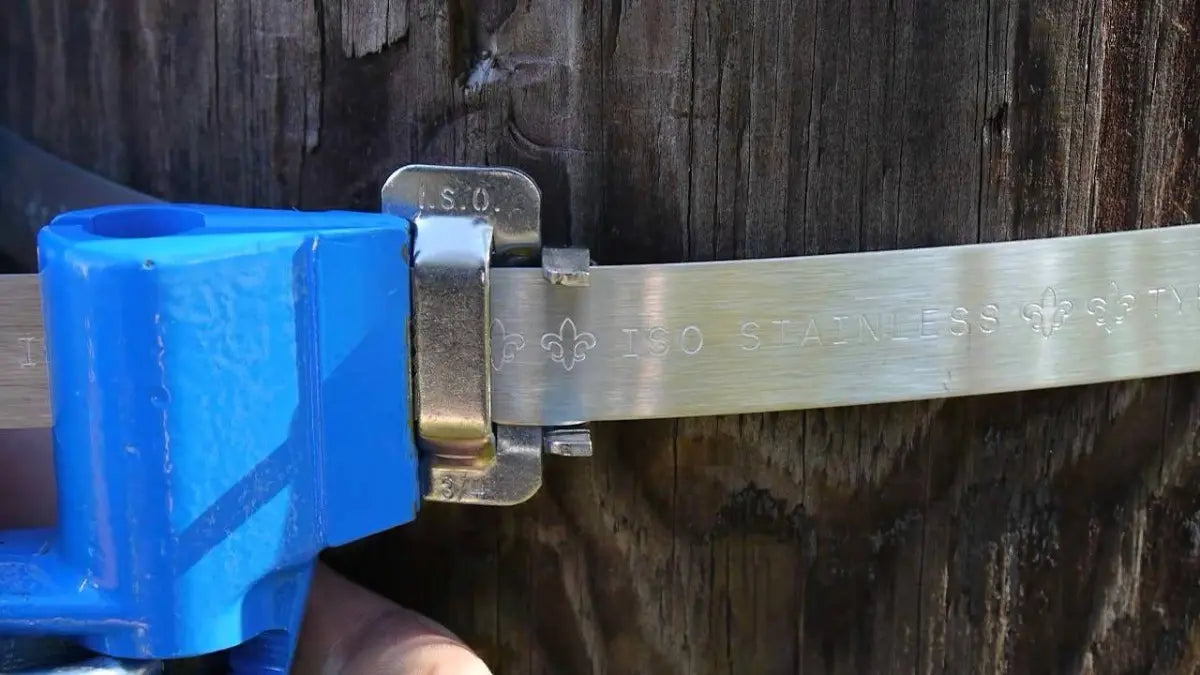 Tensador azul cerrando una hebilla de acero inoxidable sobre un fleje que rodea un poste de madera