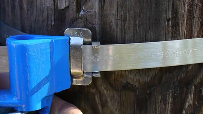 Tensador azul cerrando una hebilla de acero inoxidable sobre un fleje que rodea un poste de madera